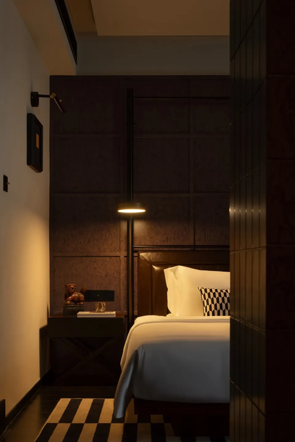 Modern minimalist bedroom with a leather headboard, wooden furniture, and fabric bedding.