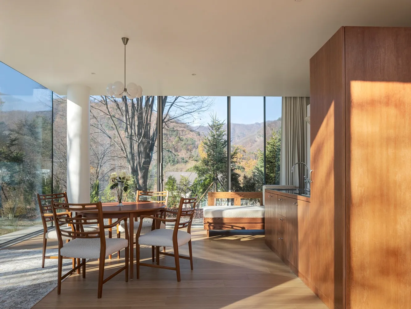 A minimalist residential kitchen featuring wood elements and a view of the mountains through floor-to-ceiling windows.