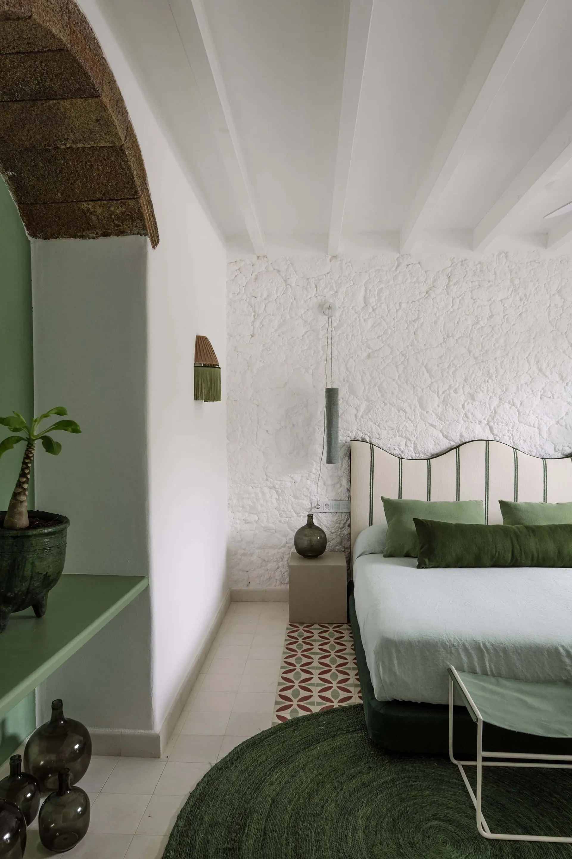 A cozy bedroom with minimalist design featuring green textiles and concrete walls.