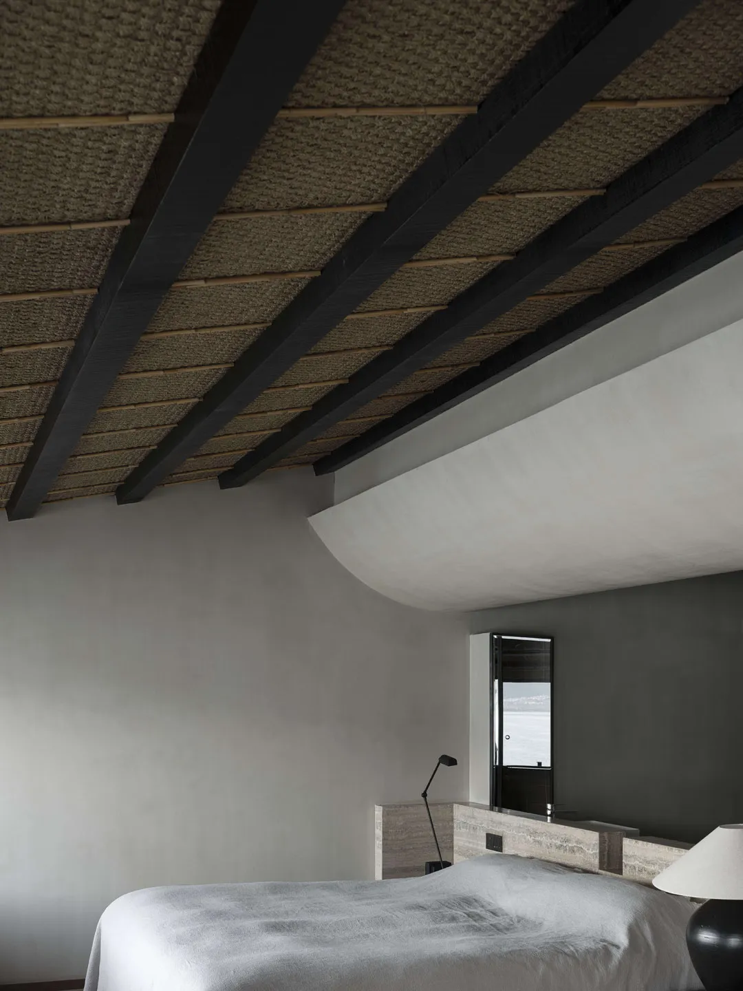 Interior of a modern minimalist bedroom featuring a concrete finish and a view of the ocean through a window.