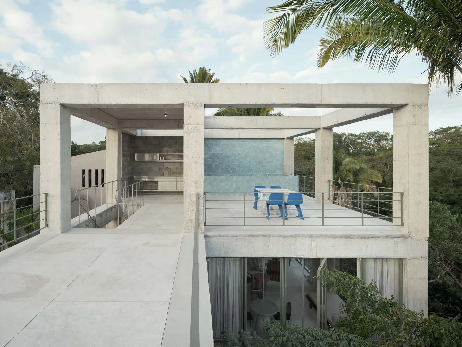 A modern rooftop deck made of concrete with a concrete wall and a blue table and chairs.
