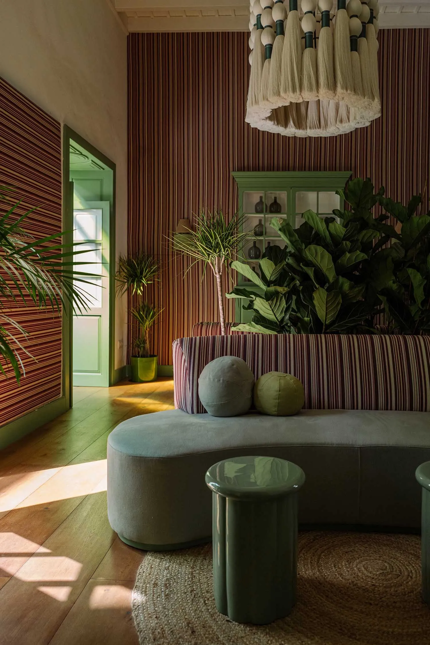 A modern living room featuring a striped sofa adorned with round cushions and surrounded by green plants and a textured cloth
