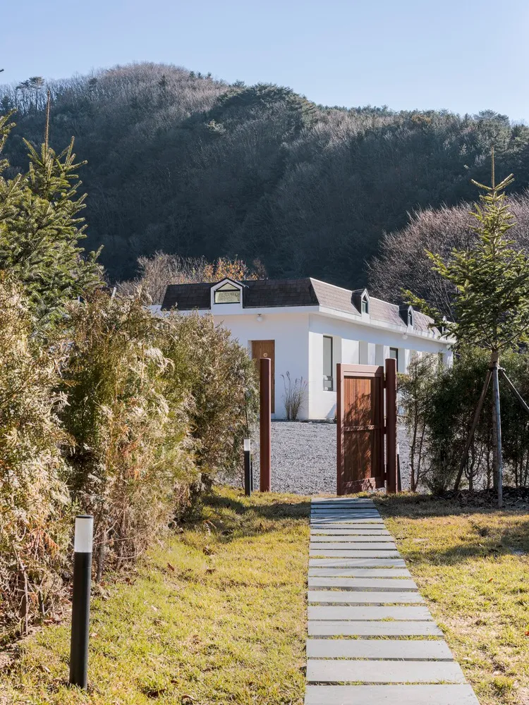A modern home with white stucco walls and black metal accents, featuring a stone pathway and a wooden gate.