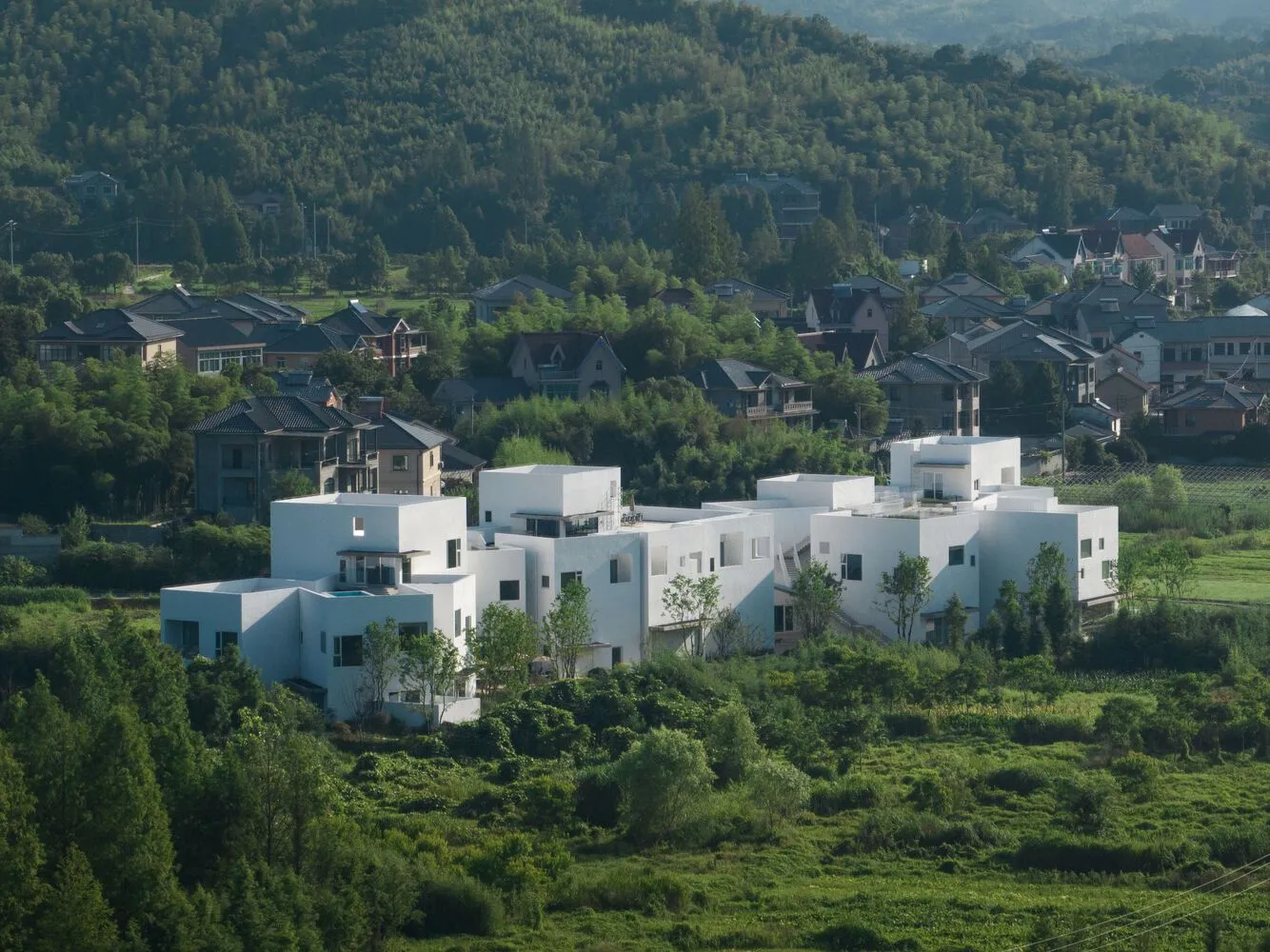 A modern residential building with white-painted concrete walls surrounded by greenery.