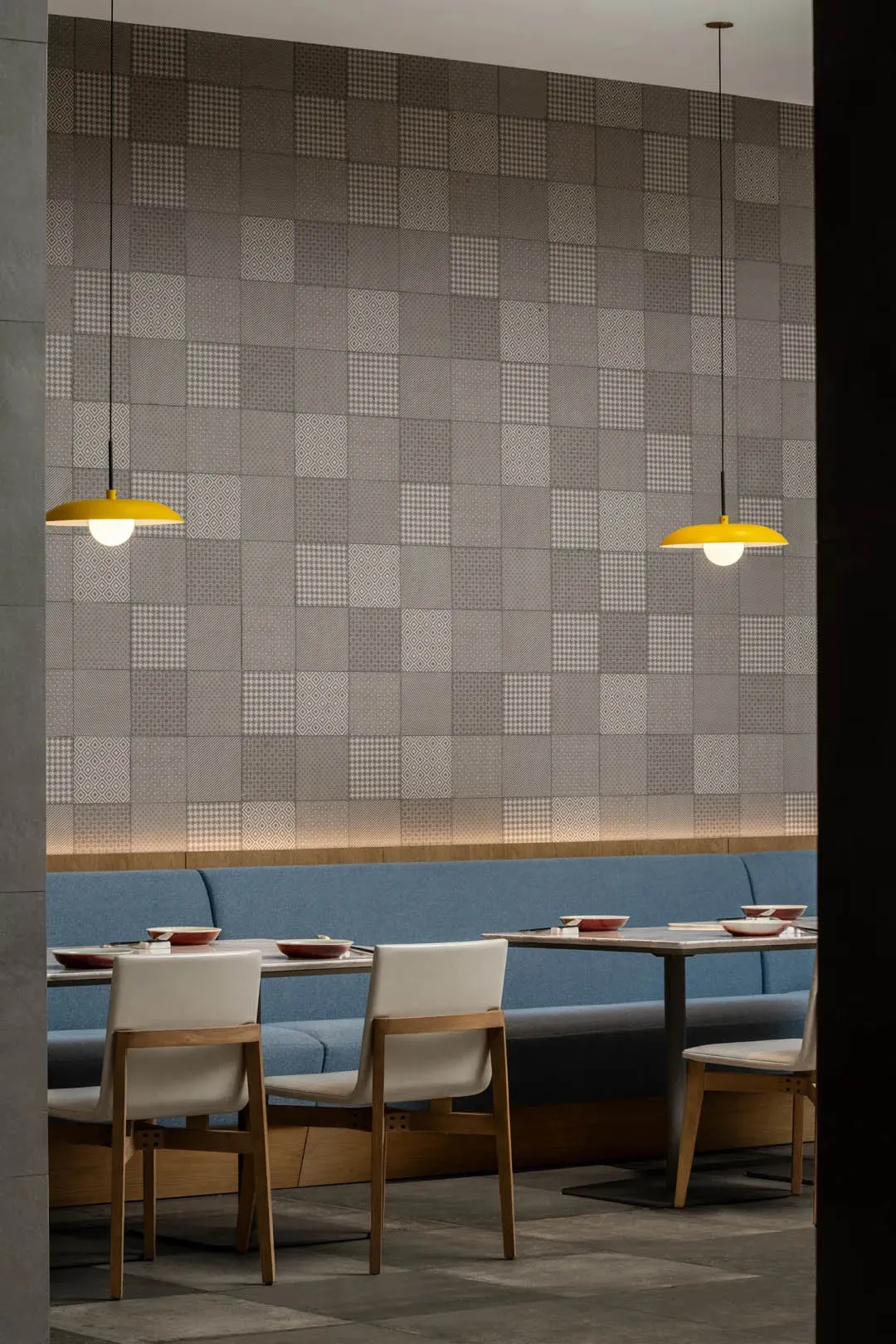 Modern restaurant interior featuring tiled walls with geometric patterns, blue booth seating, and white chairs.