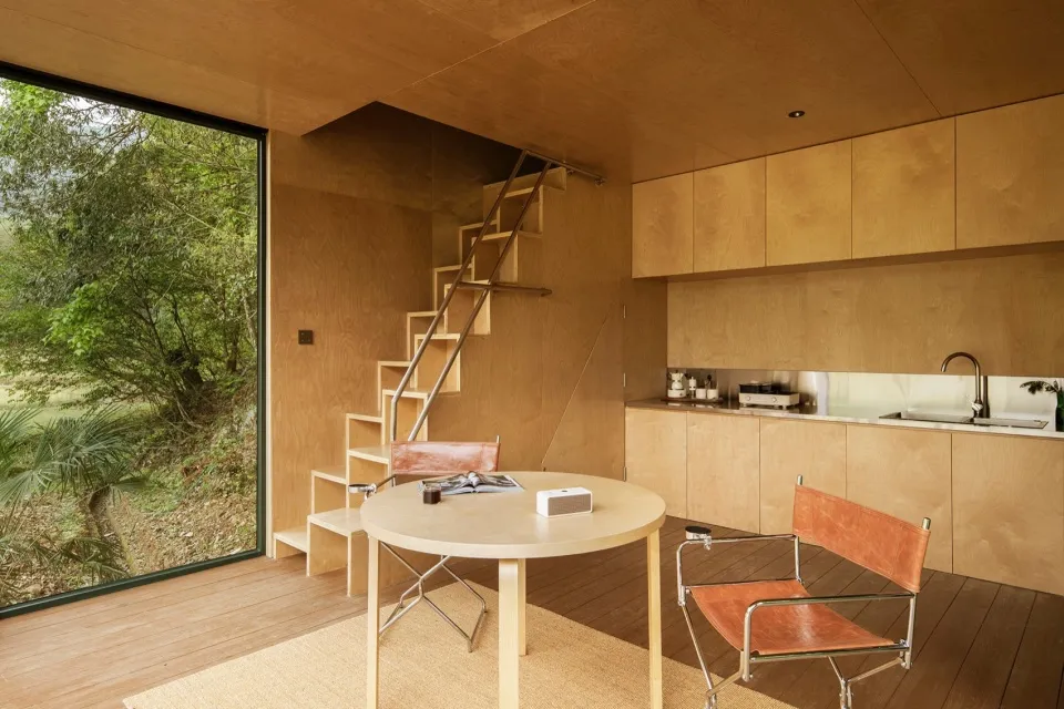 Minimalist kitchen with a natural wood finish, featuring a round table and chairs, a kitchen counter with cabinets, and a lad