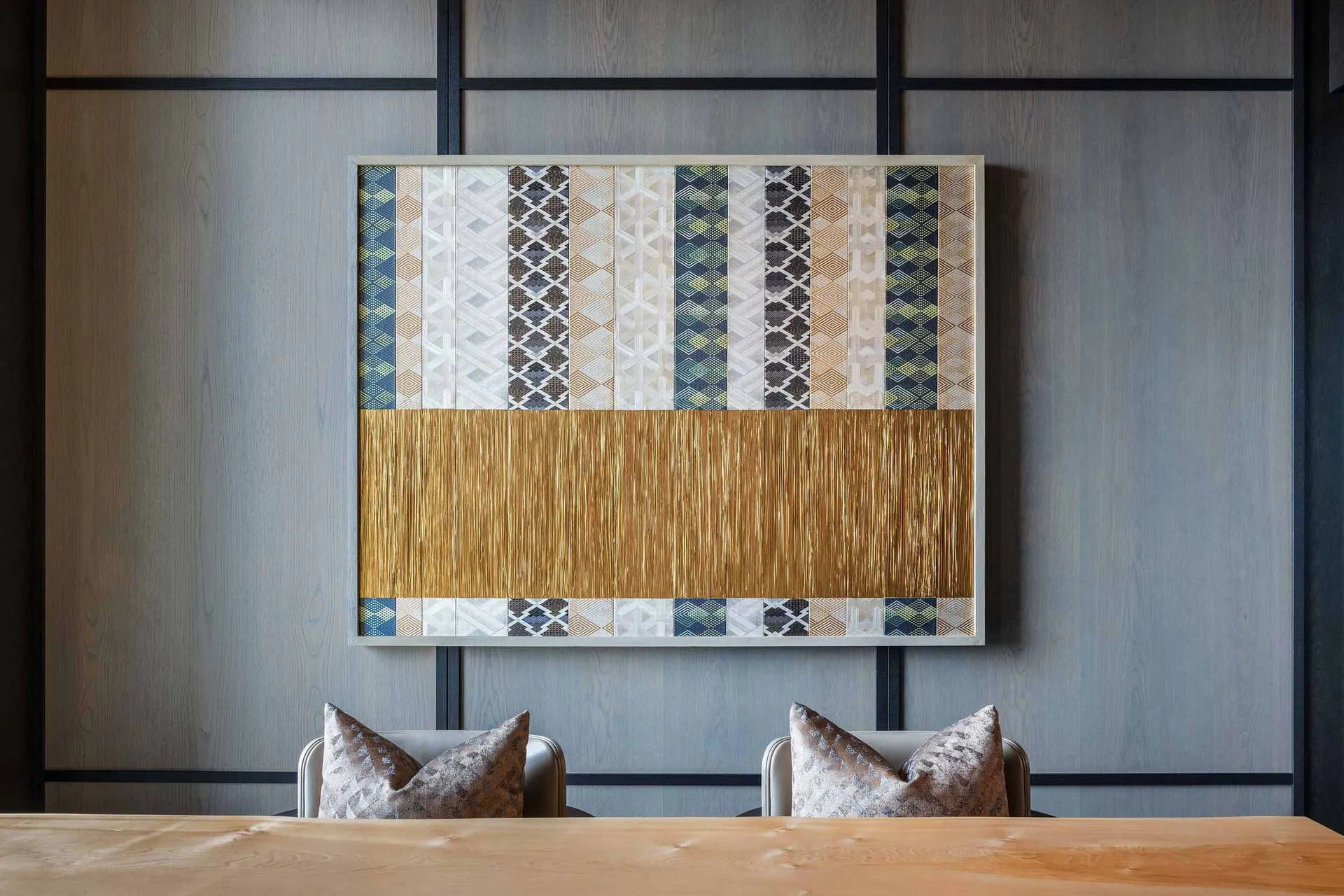 A modern dining room featuring a wall adorned with various patterned tiles in shades of beige and gold, with a wooden table a
