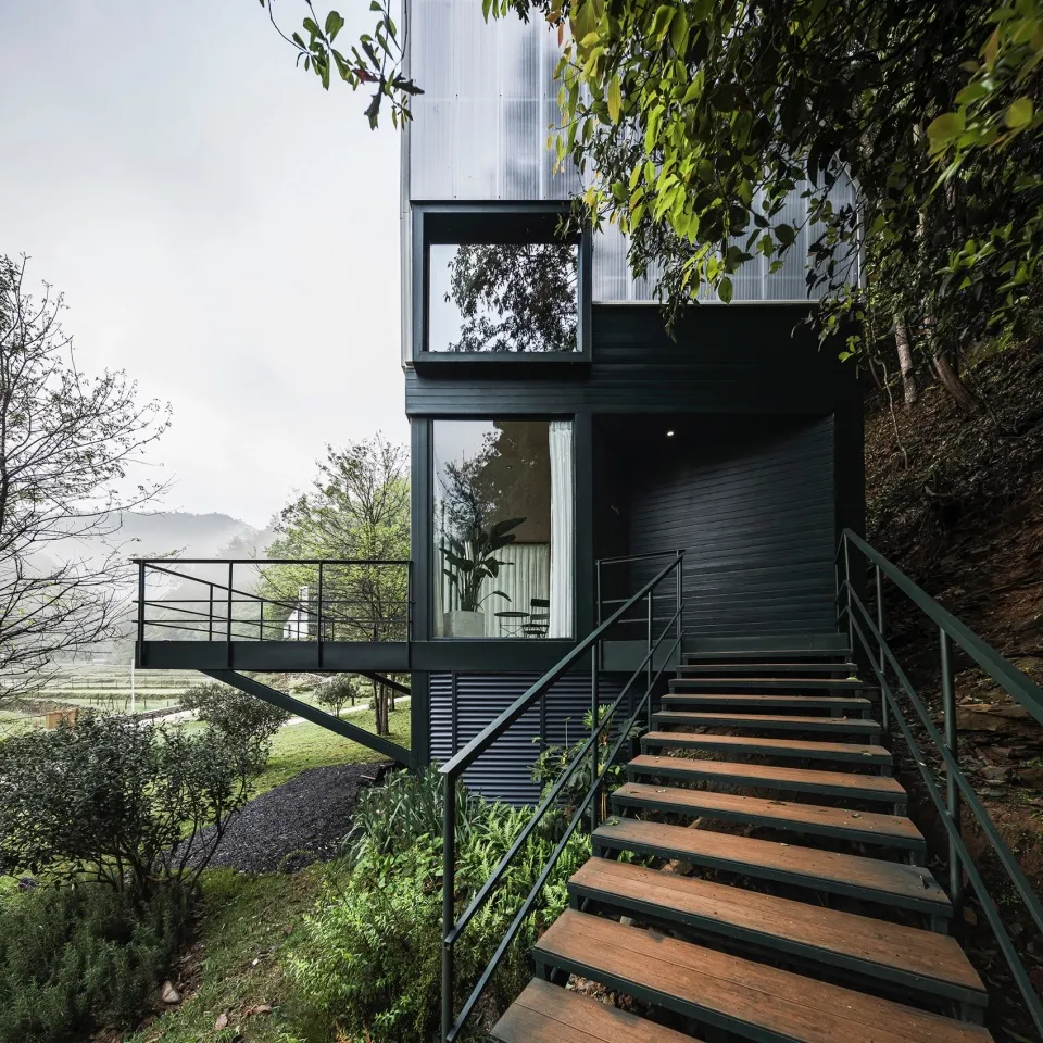 Modern house with black metal cladding, glass windows, and wooden staircase.