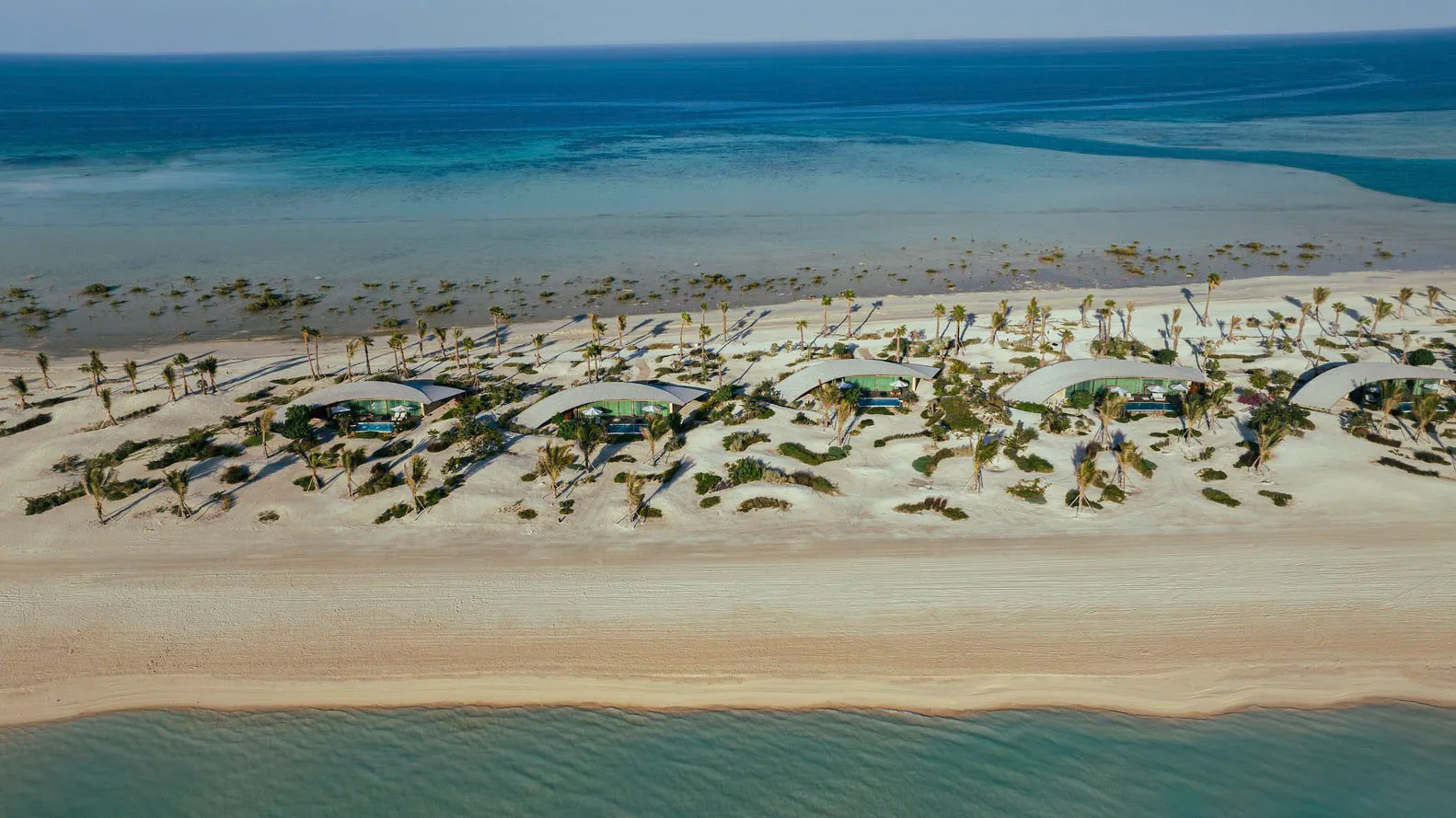 Aerial view of modern buildings on a sandy beach with clear blue waters.