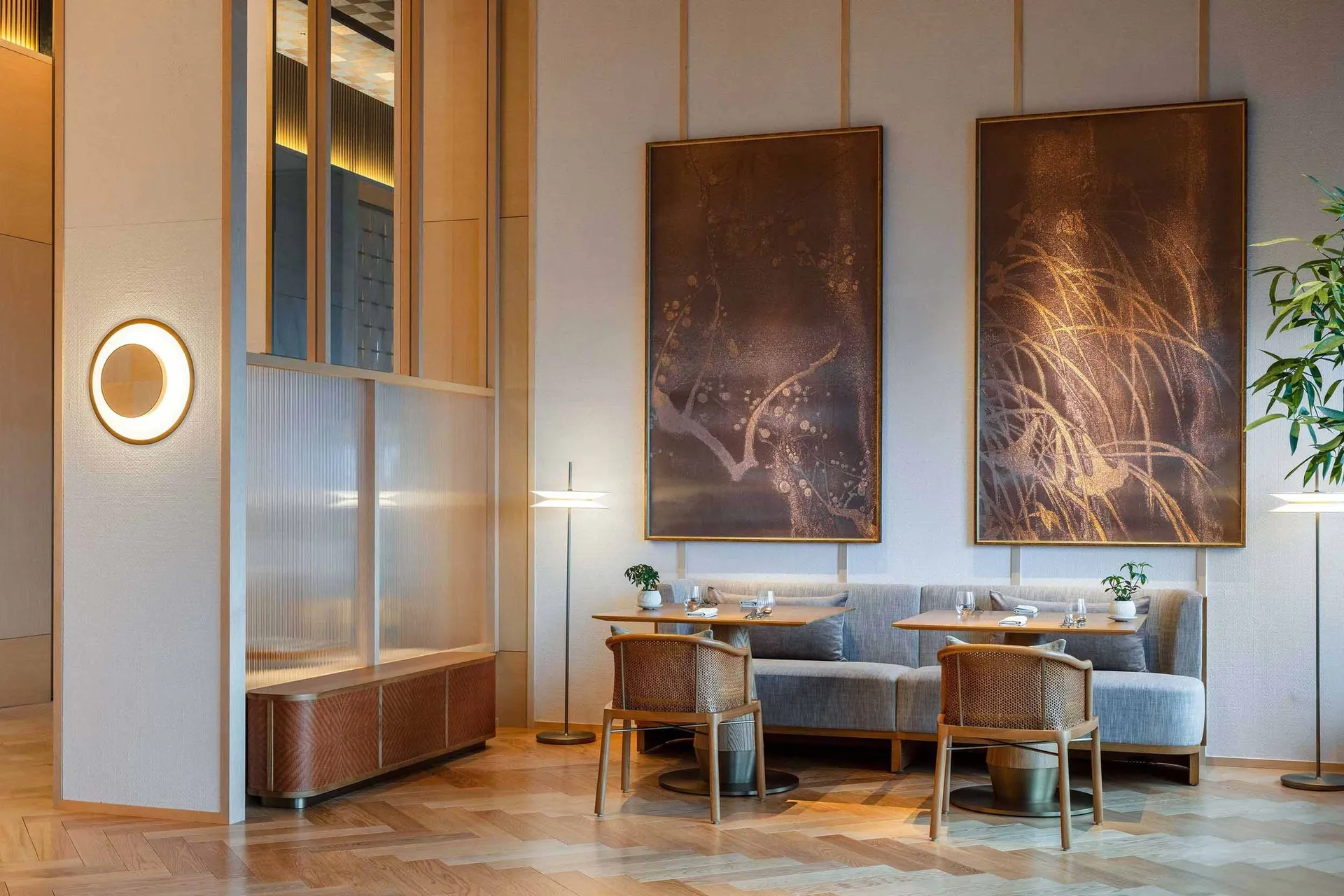 A modern restaurant interior with wooden furniture, featuring a seating area with tables, chairs, and large artwork on the wa