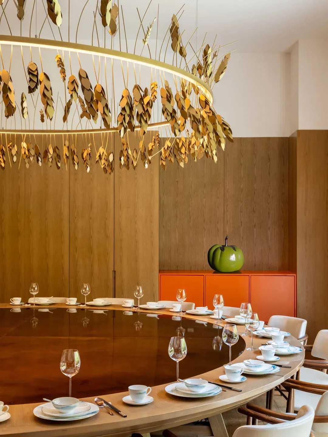 A modern restaurant interior with wooden furniture, featuring a large round table set for dining, a golden chandelier hanging