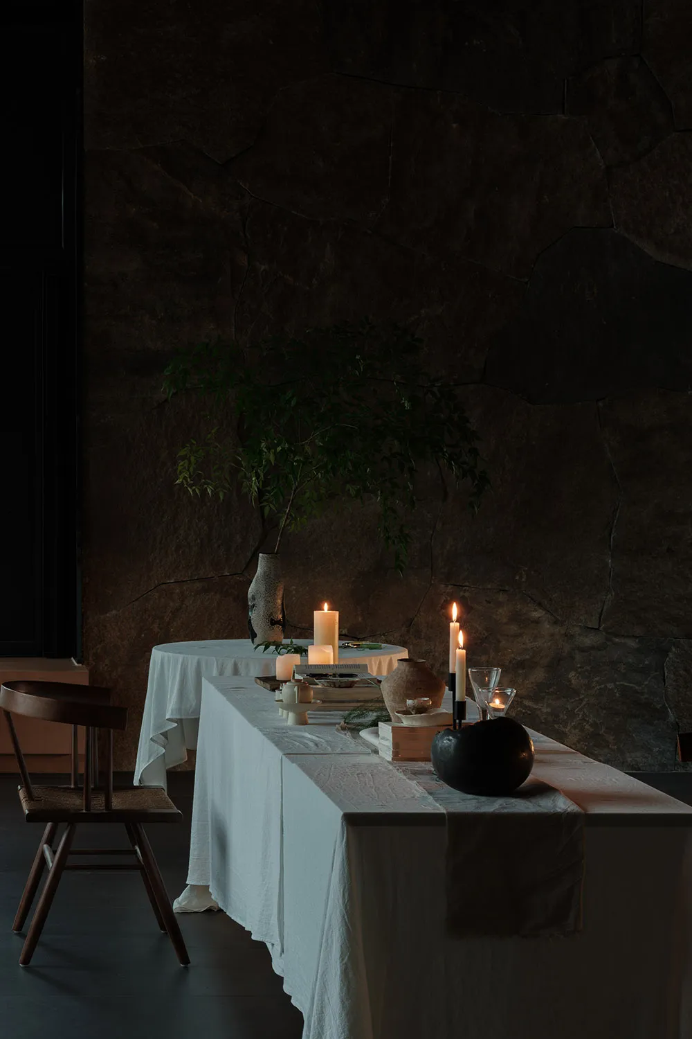 A minimalist interior setting featuring a stone, wooden, and linen table with candles and decorative elements.