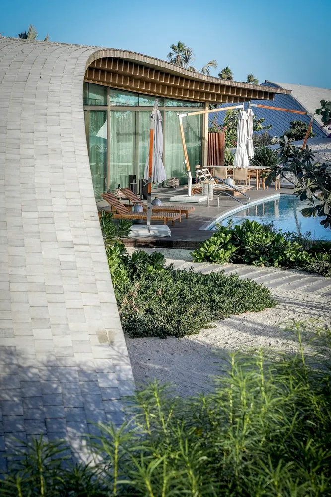 A modern, minimalist exterior residential home featuring glass and wood materials with a curved architectural design.