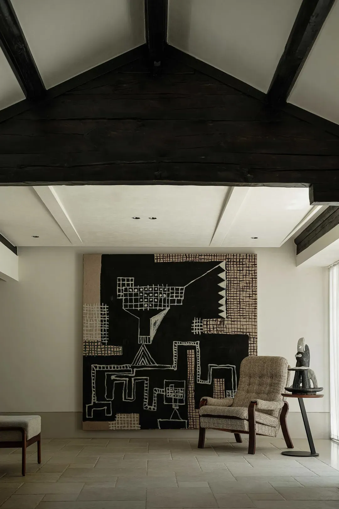 A modern interior with a black patterned tapestry, featuring a geometric design and minimalist chair with a wood frame.