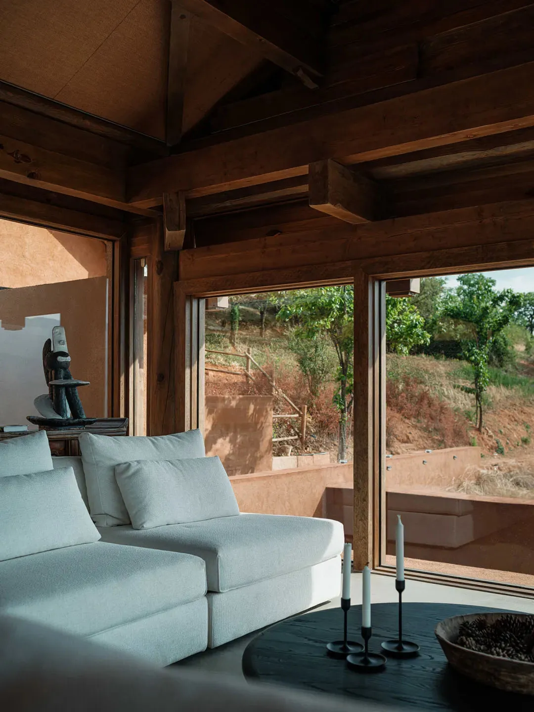 A modern living room with a white sofa, concrete floor, and large windows overlooking a natural landscape.