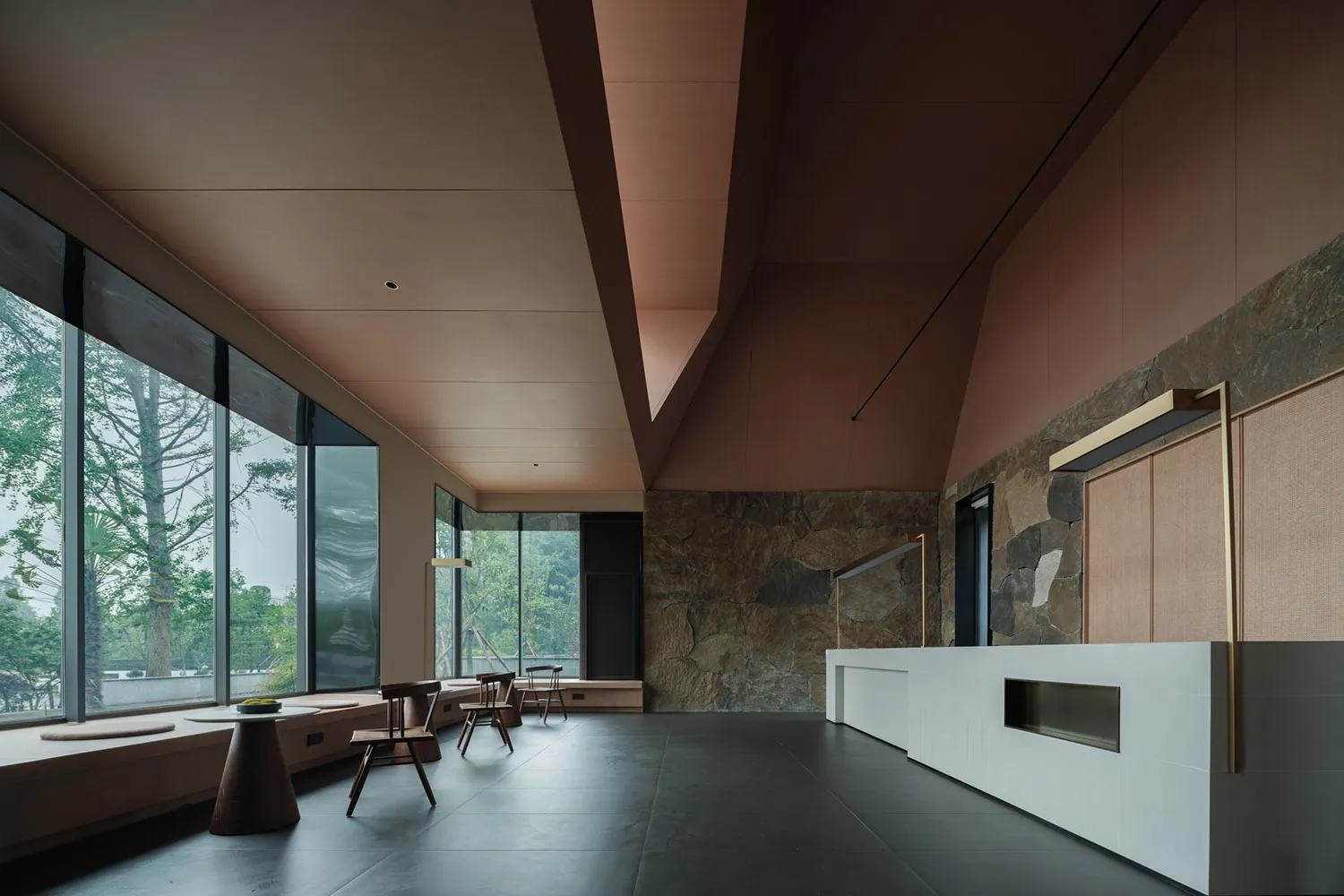 A modern lobby with concrete walls and floor, featuring minimalist furniture and a reception desk.