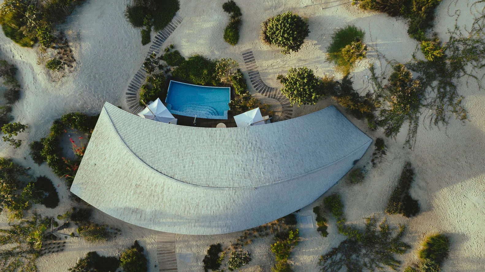 An aerial view of a modern residential structure with a curved roof and tiled materials.