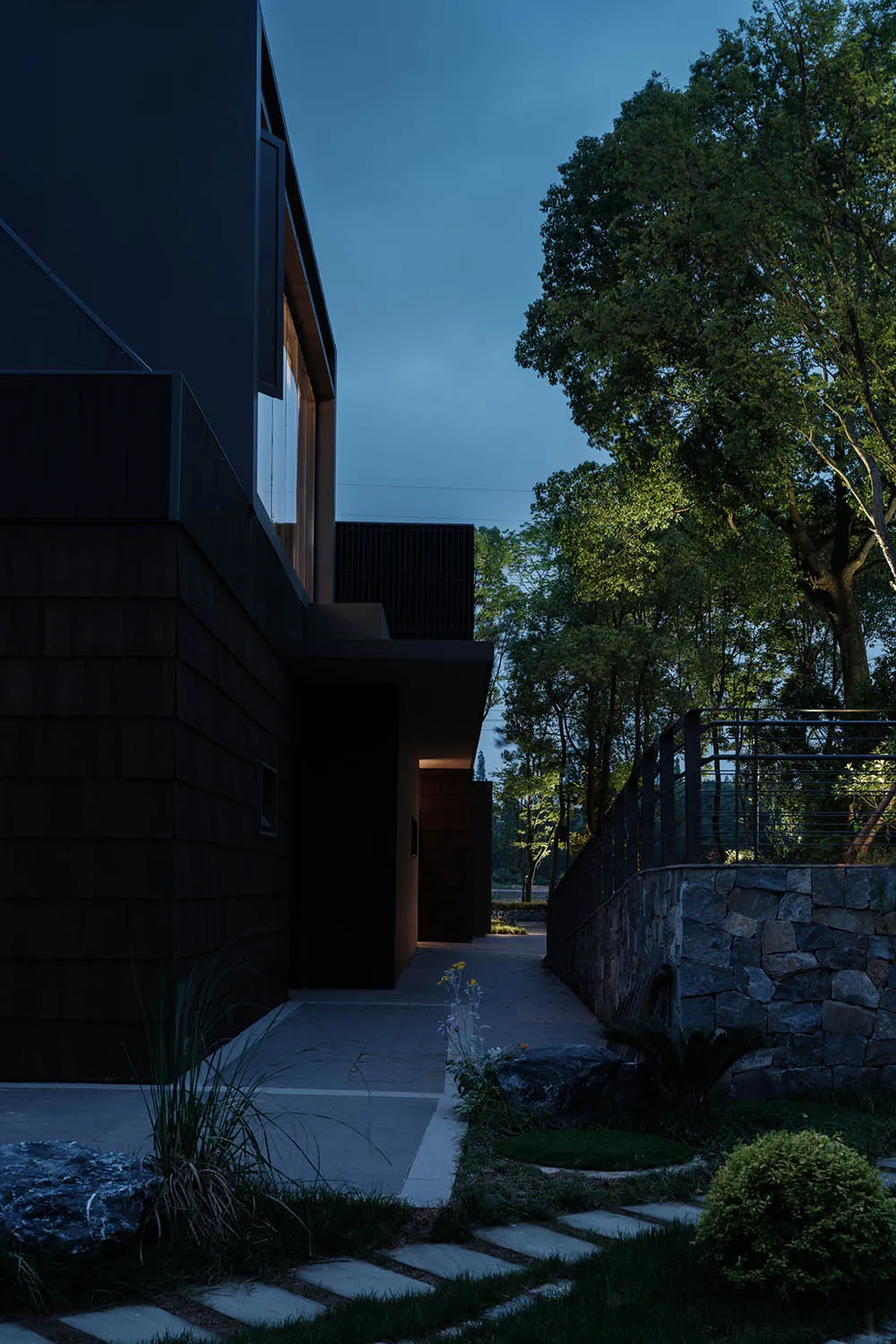 Modern residential exterior with concrete and glass materials, illuminated by soft ambient lighting.