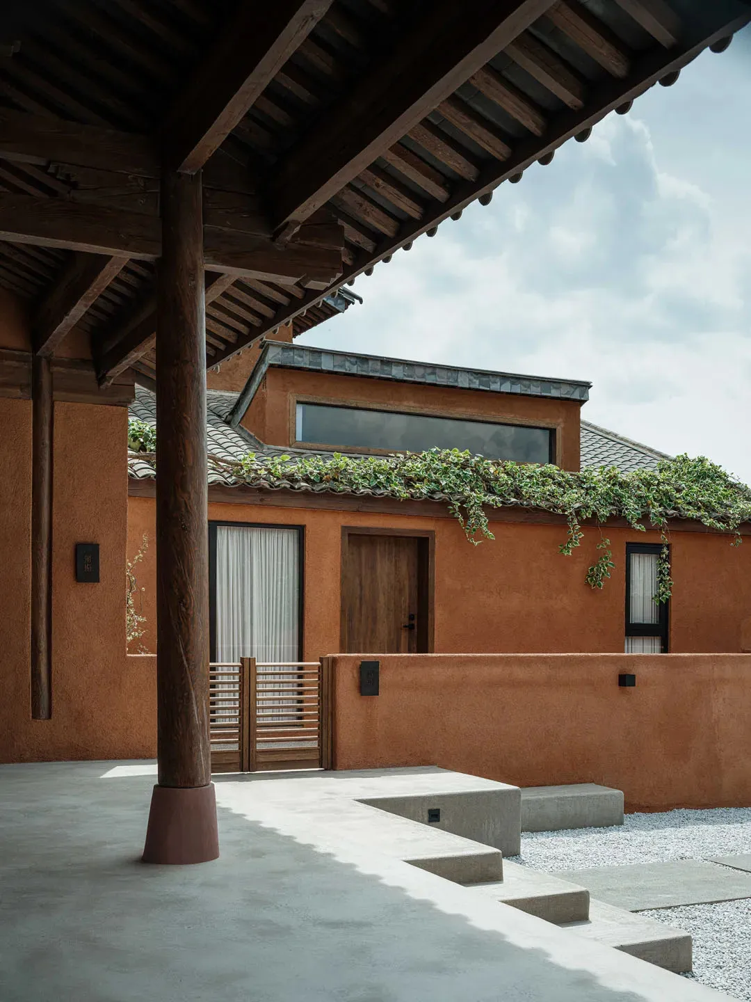 Modern residential exterior with terracotta clay walls and a metal roof structure.
