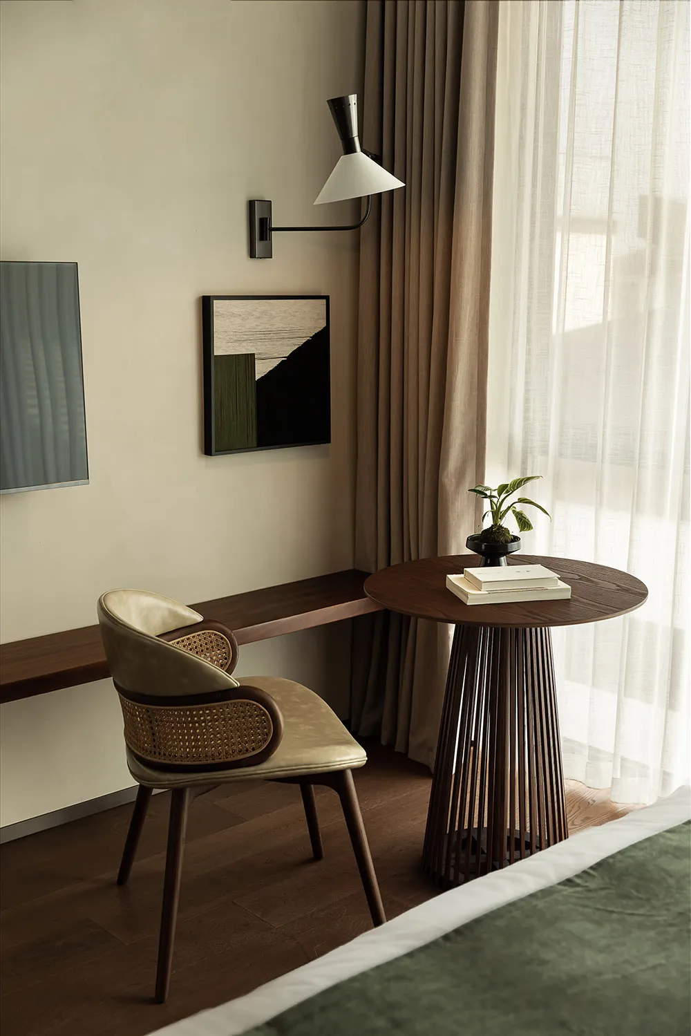 A modern minimalist bedroom featuring a wooden table with a plant and books, a comfortable chair, and a sleek desk lamp.