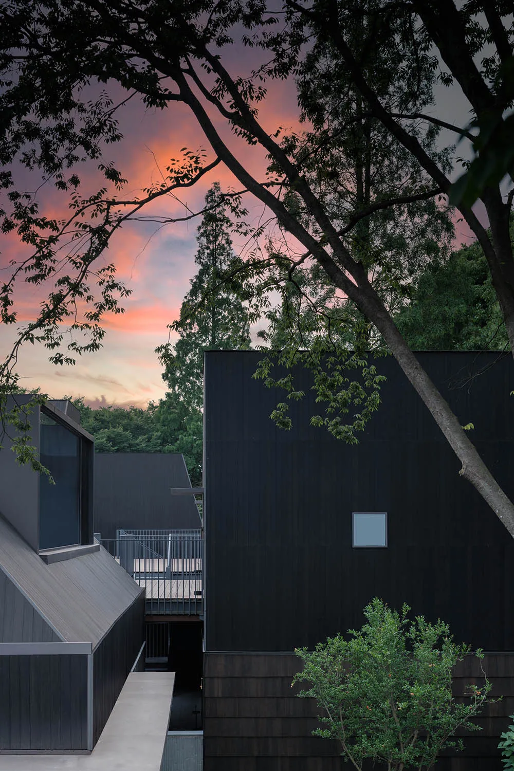 Modern exterior featuring sleek, black metal-clad panels under a dramatic, sunset sky.