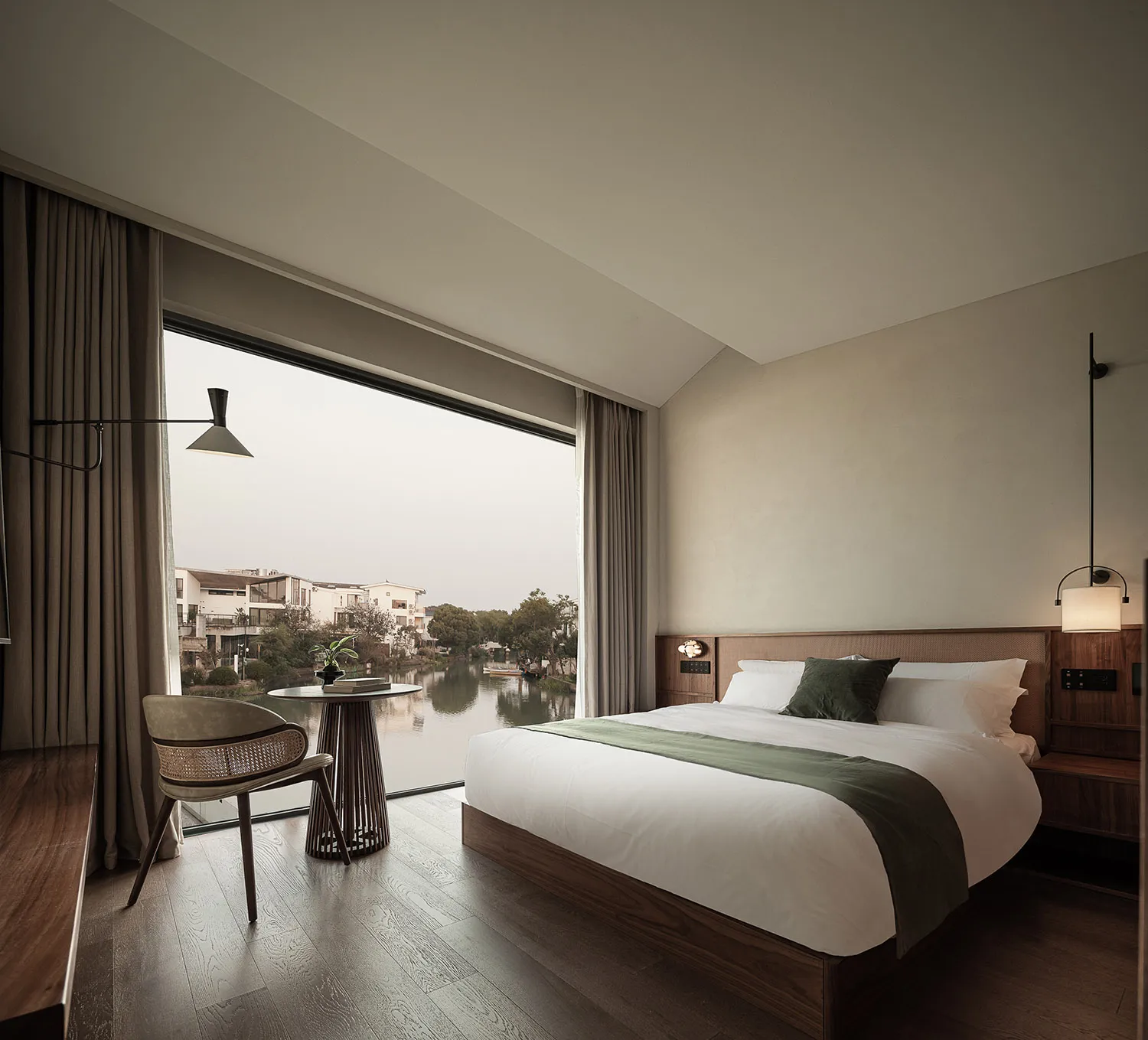 A modern bedroom featuring a cozy bed with white bedding, green throw pillows, and a wooden floor, looking out onto a scenic