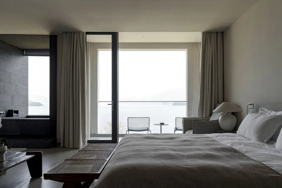 A minimalist bedroom with a large bed, stone walls, and fabric textiles.