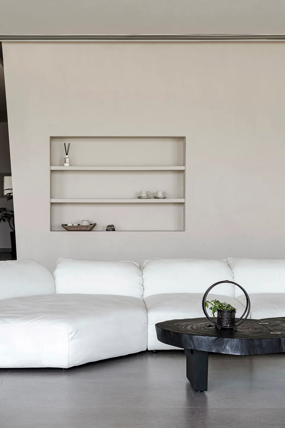 A minimalist living room with a large white sofa and a black coffee table on a concrete floor.