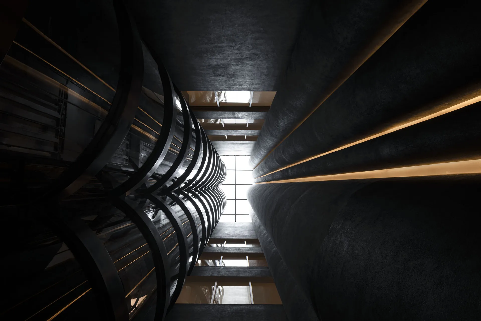 A black metallic staircase with curved railings inside a building with high ceilings and natural light.