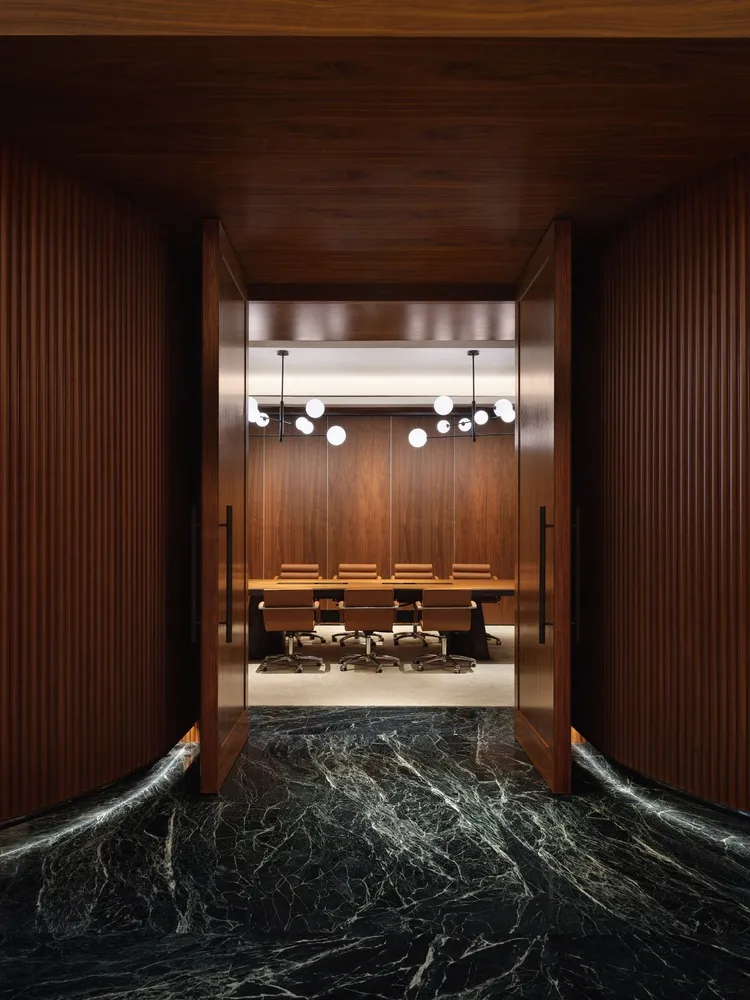 A modern conference room with wooden paneling and marble furniture, featuring a long table surrounded by chairs and illuminat