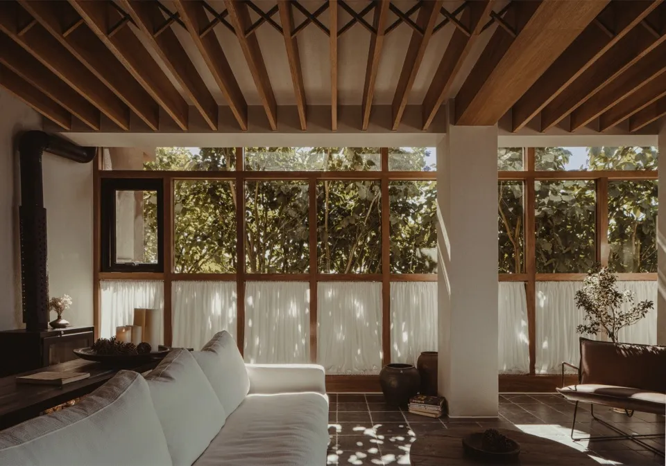 Minimalist living room with white furniture and large windows, featuring wooden elements and natural light.