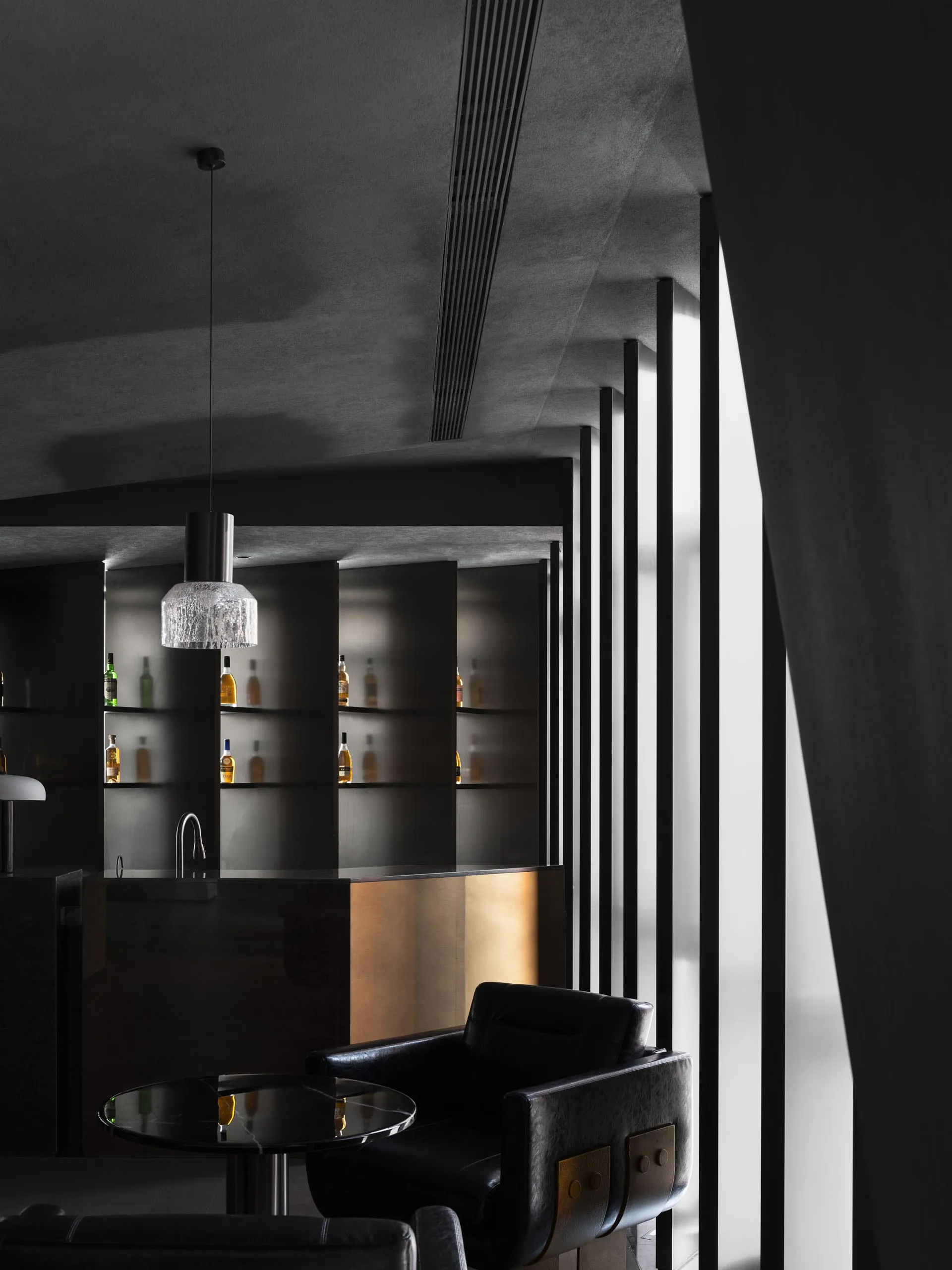 A modern hotel suite bar featuring black walls, metal accents, and a large window.