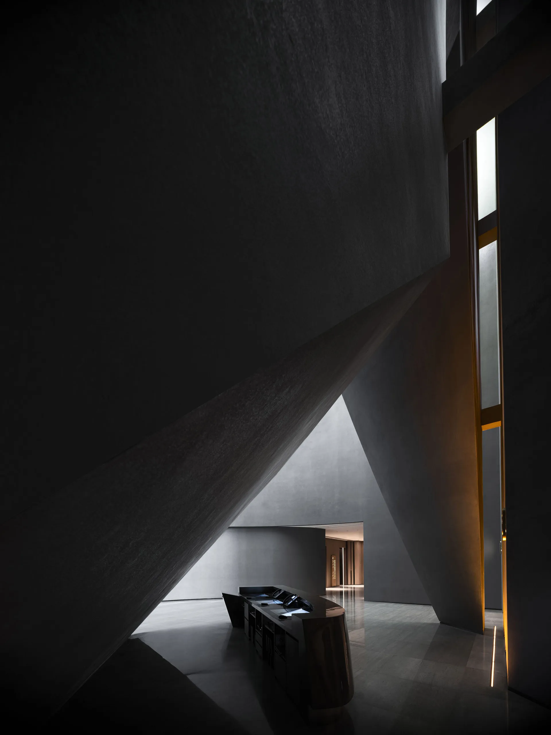 A minimalist hotel reception area with concrete walls and a sleek, black reception desk.