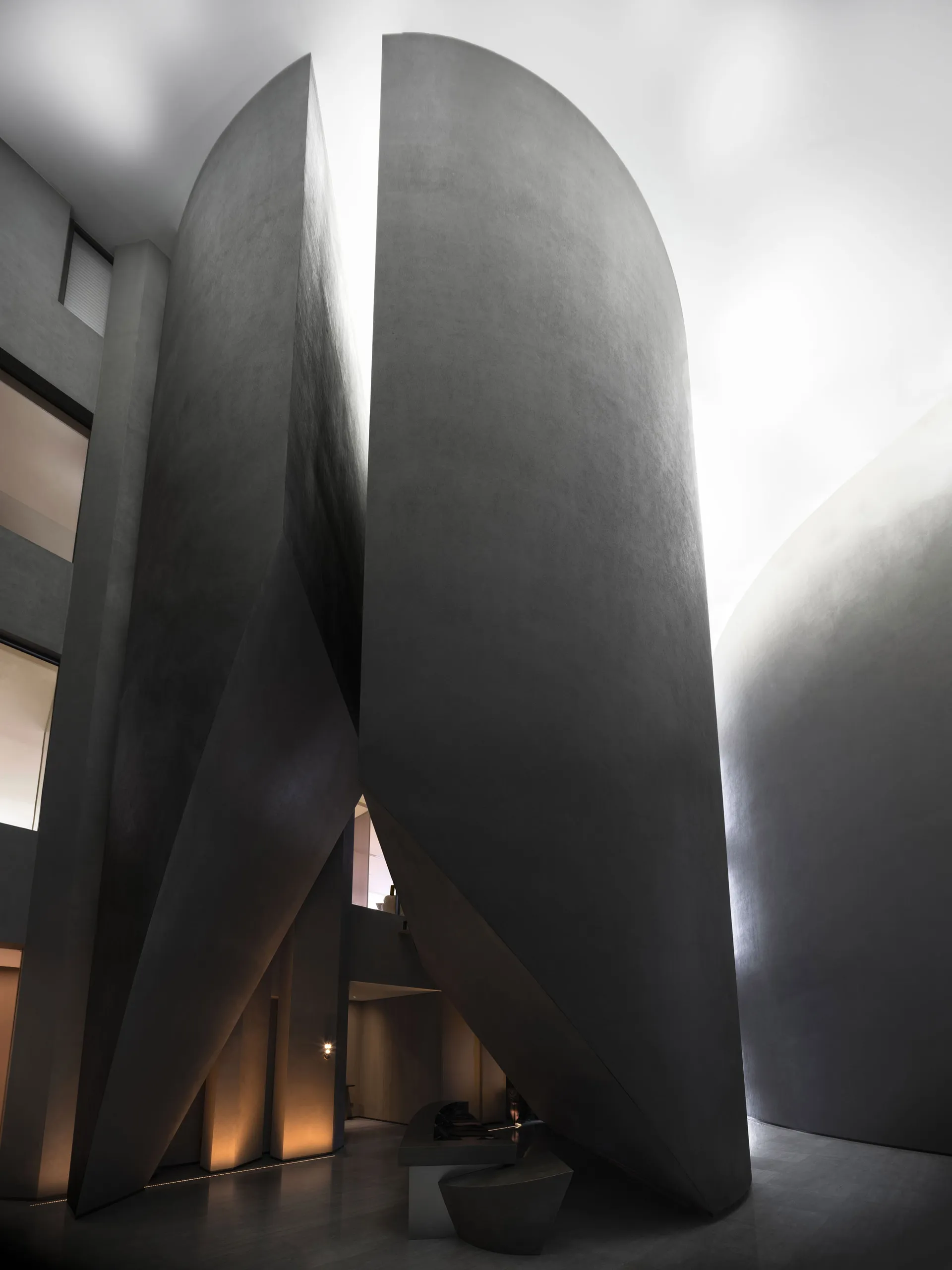 A modern monolithic concrete interior with large, curved, dark-gray walls and a geometric staircase.