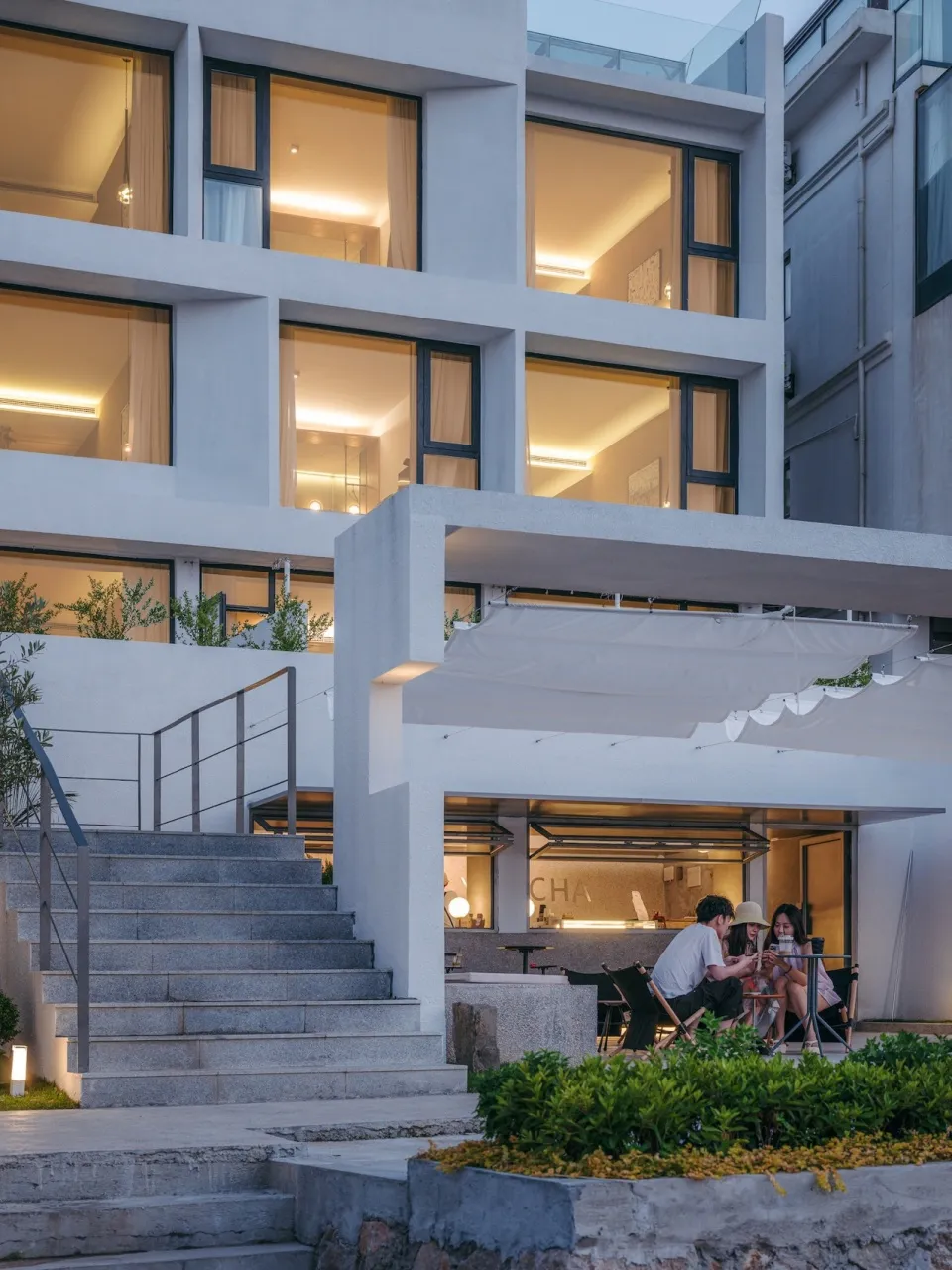 Modern residential exterior features concrete stairs, glass windows, and illuminated interior.