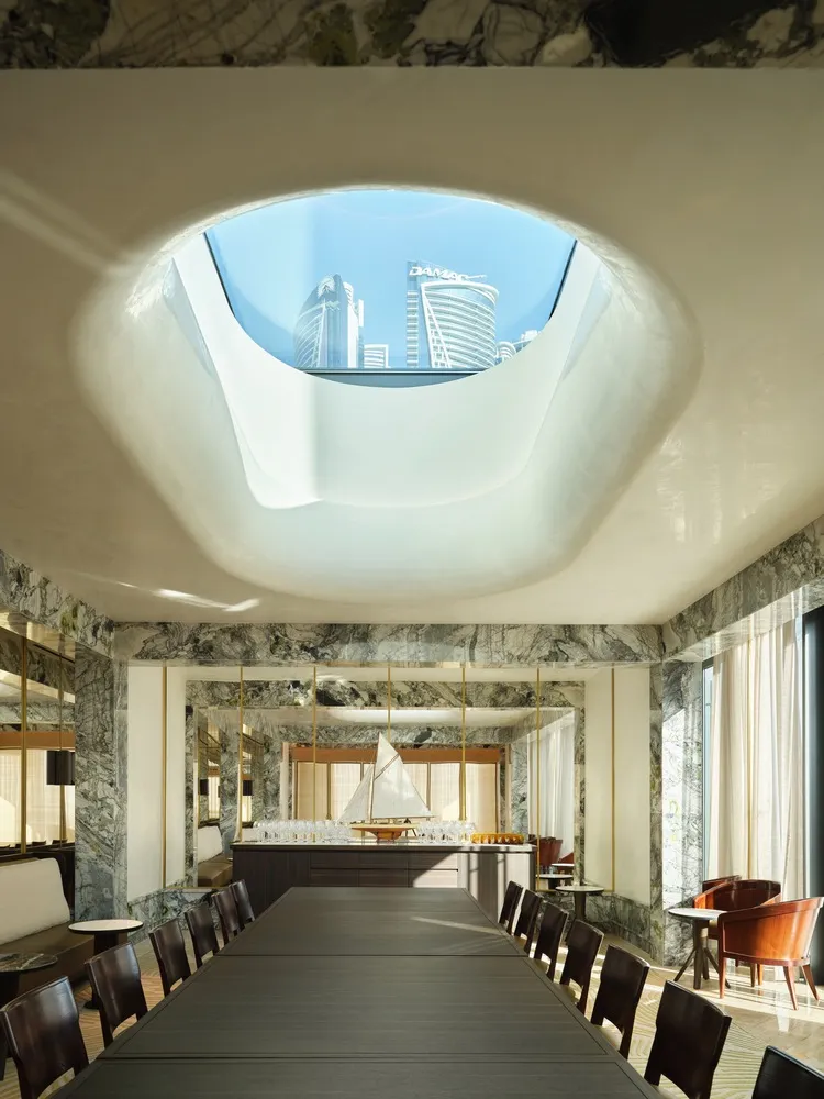 A modern restaurant interior with marble walls and a large skylight.