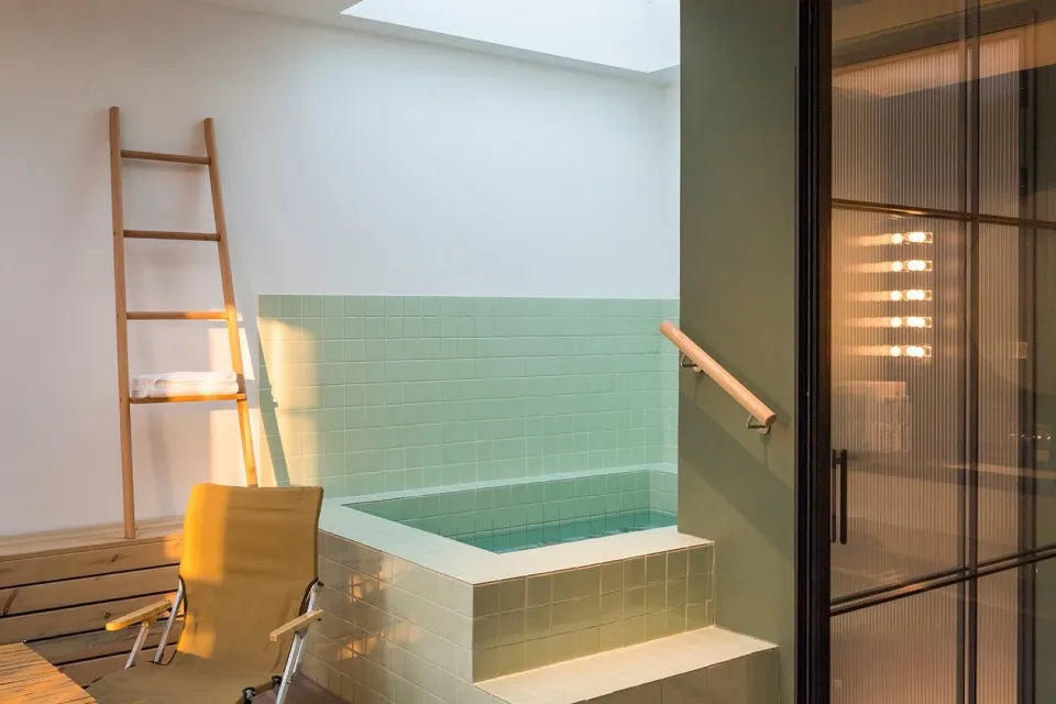 Industrial-style bathroom with green tiled walls and a wooden ladder.