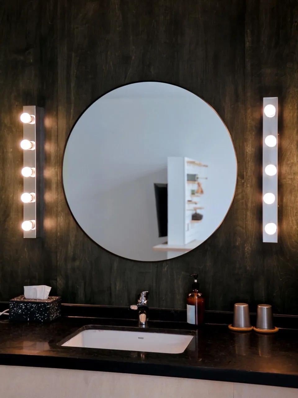 A modern industrial bathroom featuring dark wood paneling and metal lighting fixtures.