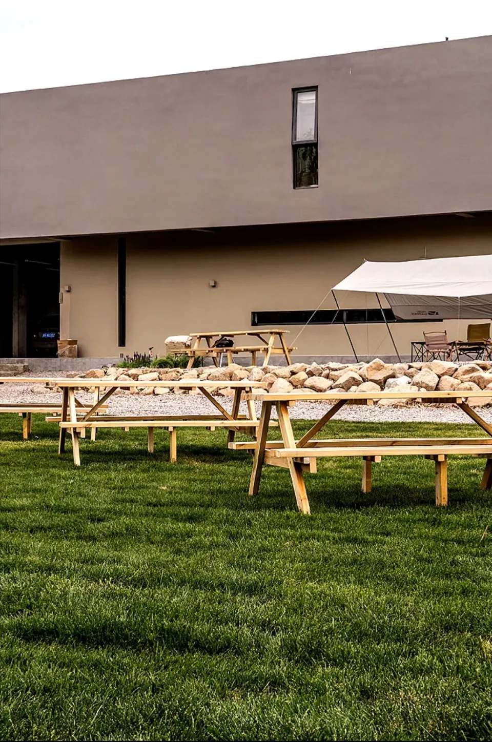 An outdoor event space featuring wooden tables and picnic benches on a grassy area.