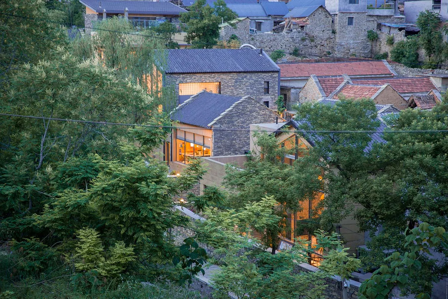A stone building with illuminated windows amidst greenery.