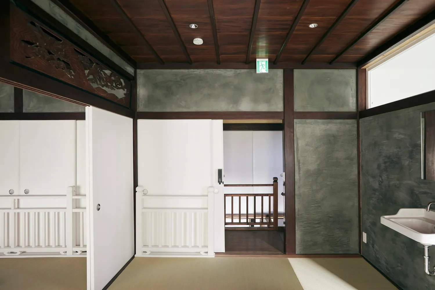 A traditional Japanese interior with wooden walls and doors, tatami mats, and a sink.