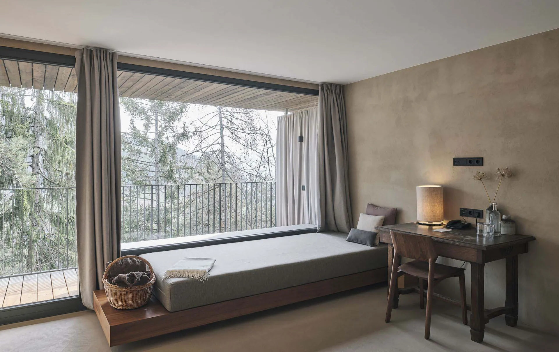 Modern bedroom with a floating bench, wooden beams, and a view of the forest through large windows.