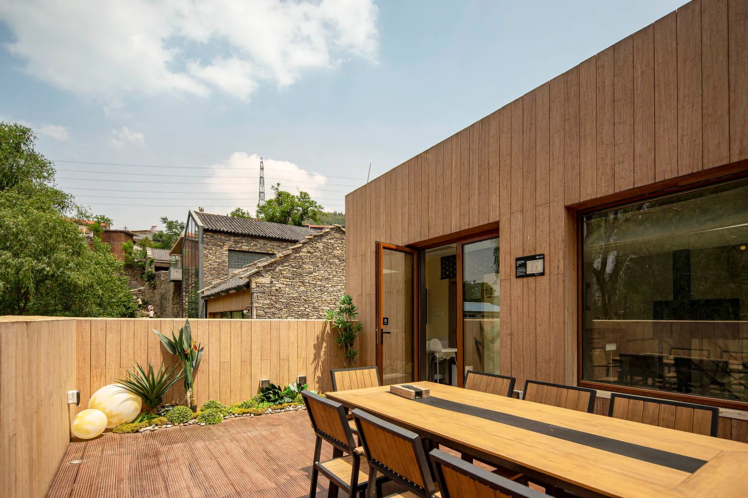 Modern exterior with wooden fence, table, and chairs in a landscaped area.