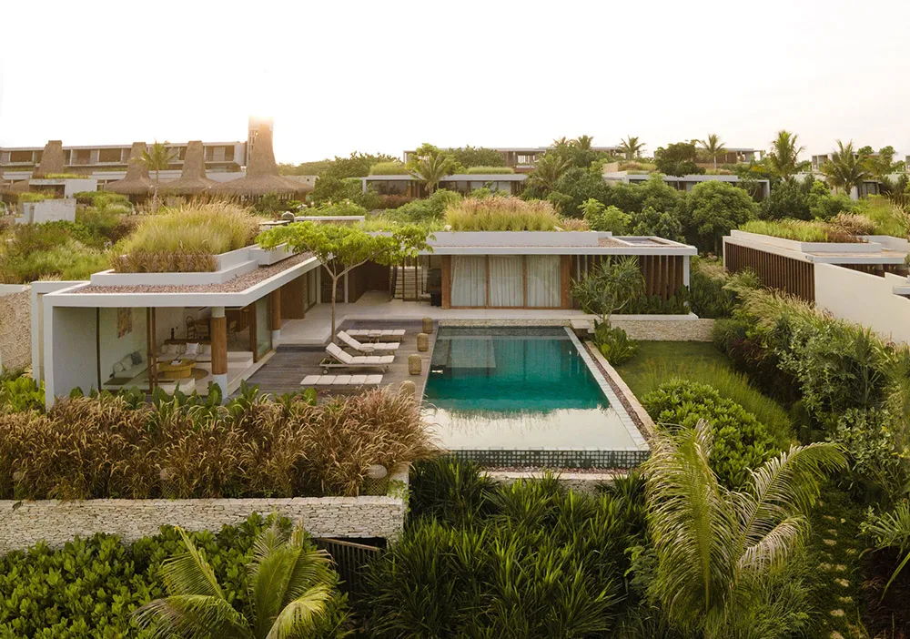 Modern outdoor living space with natural earth tones, featuring a pool, lounge chairs, and greenery.