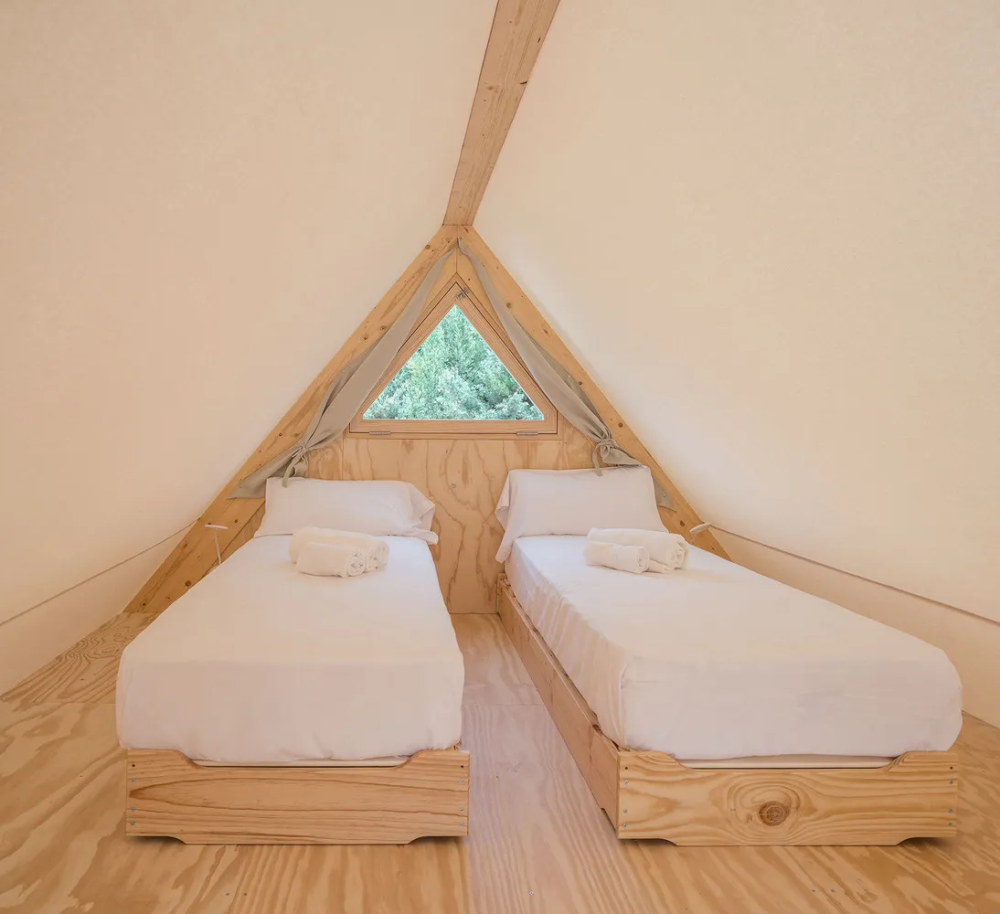 A minimalist bedroom with triangle-shaped windows, featuring twin beds with white bedding and natural wooden elements.
