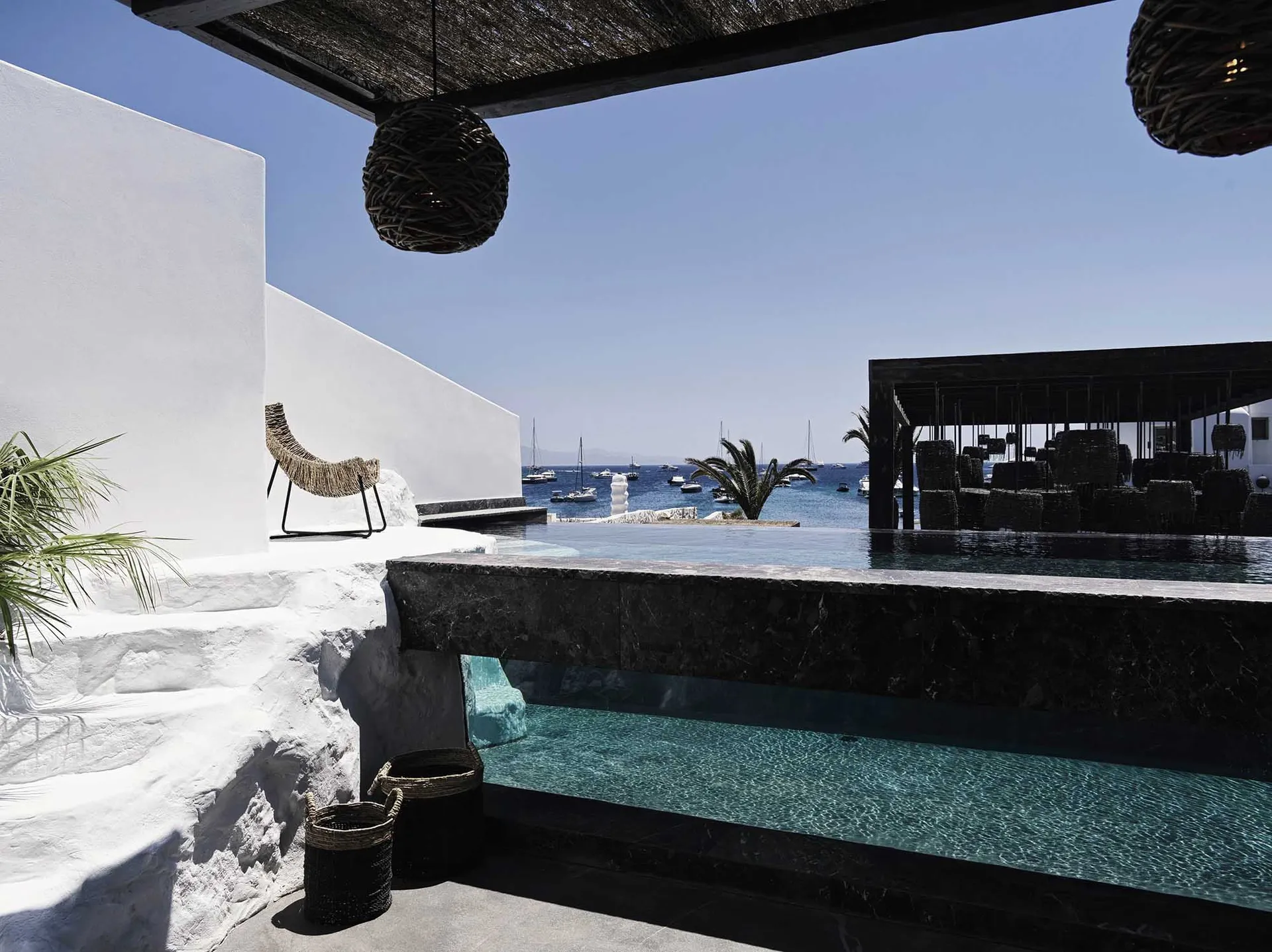 Concrete and marble vacation poolside area with lounge chairs and boats in the background.