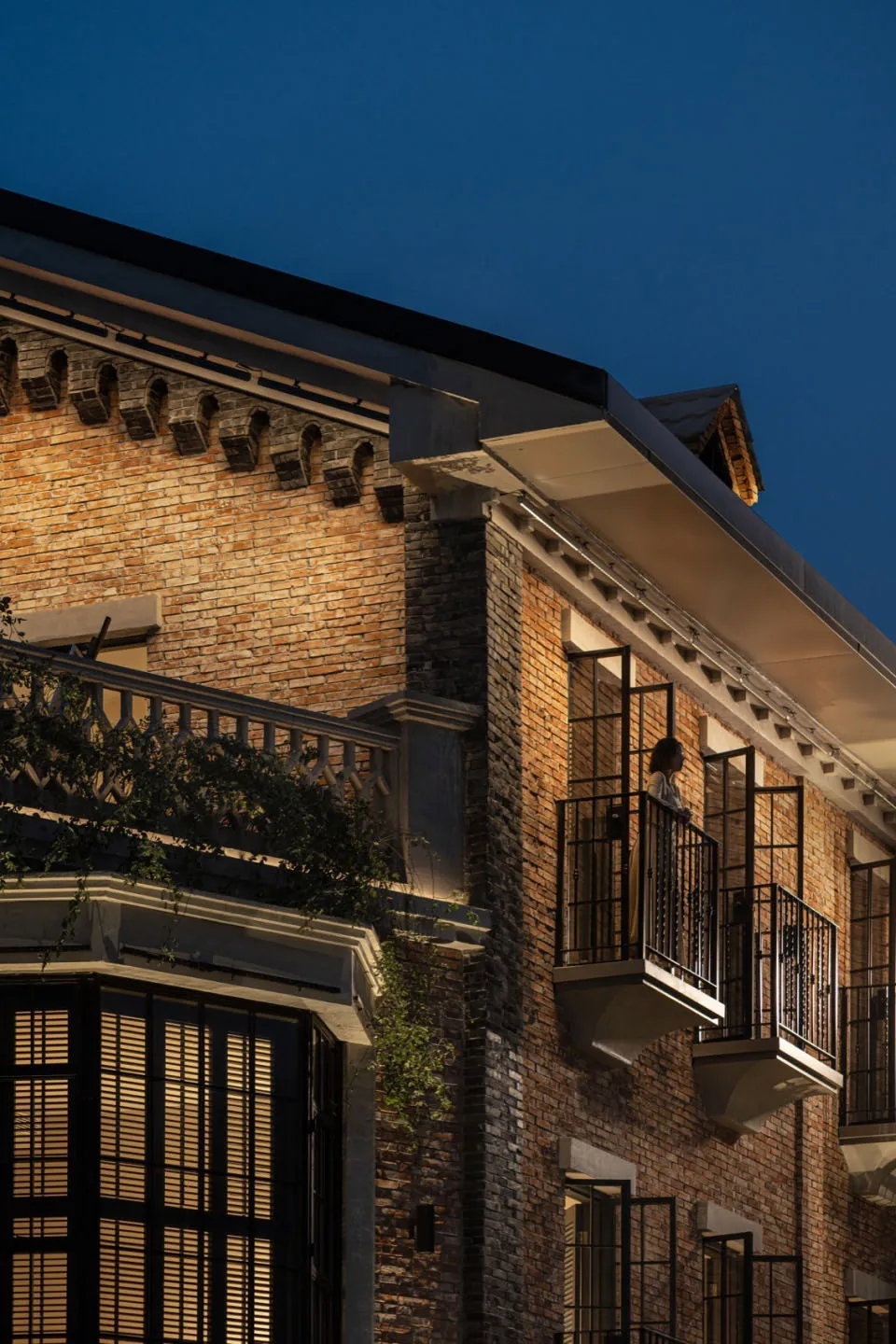 A cozy brick building at night with a person standing on a balcony