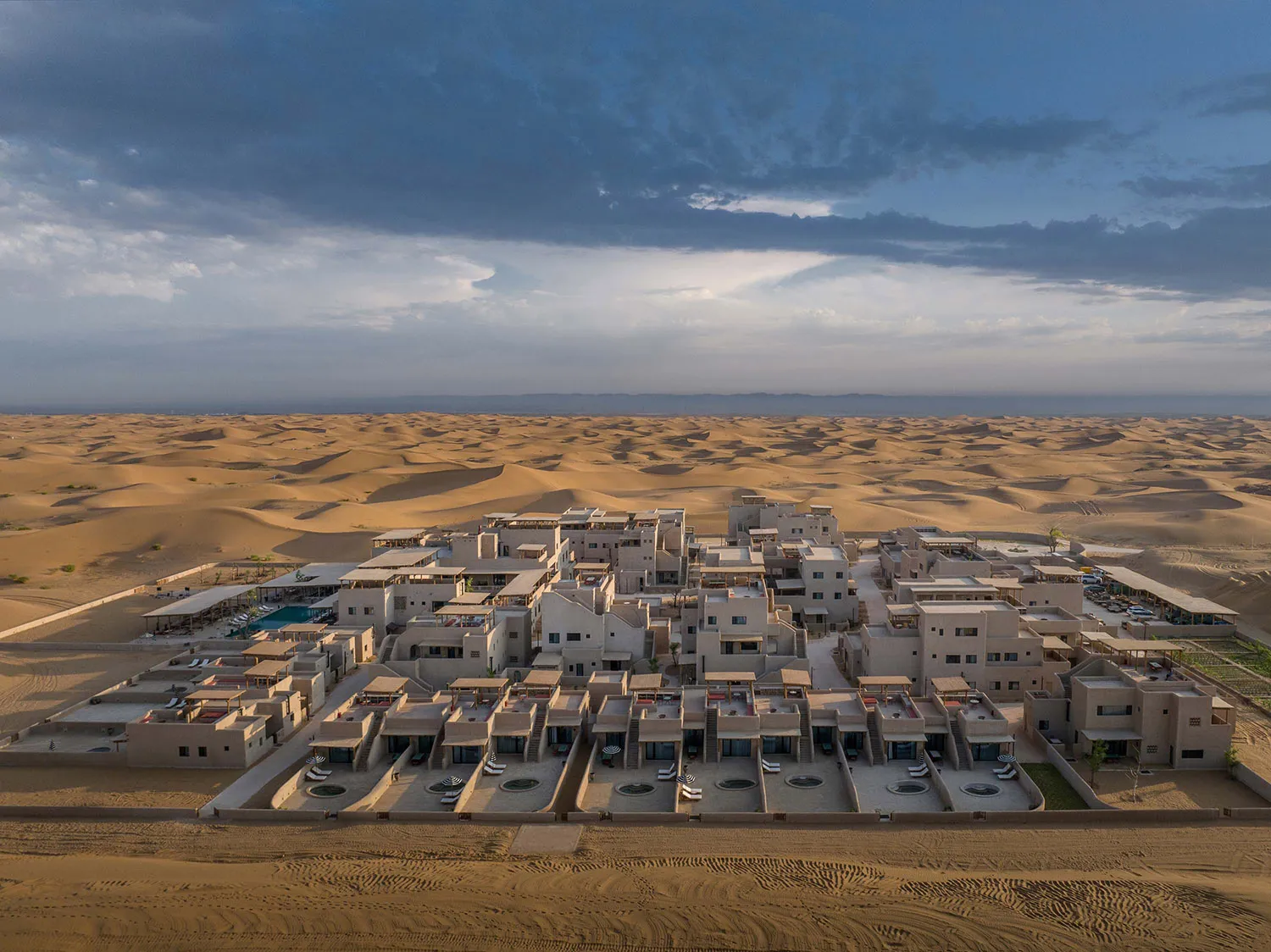 Aerial view of a resort complex in the desert, featuring numerous buildings and structures made of sand.