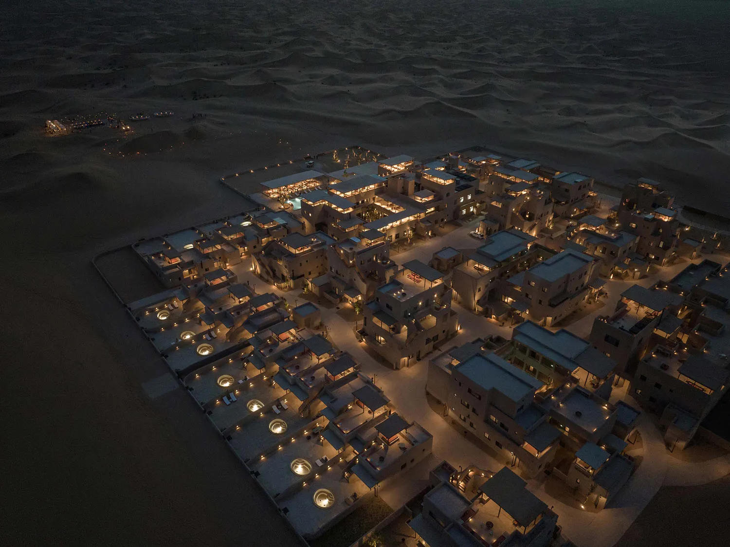 An aerial view of a luxurious resort constructed with stone materials in a desert environment at night.