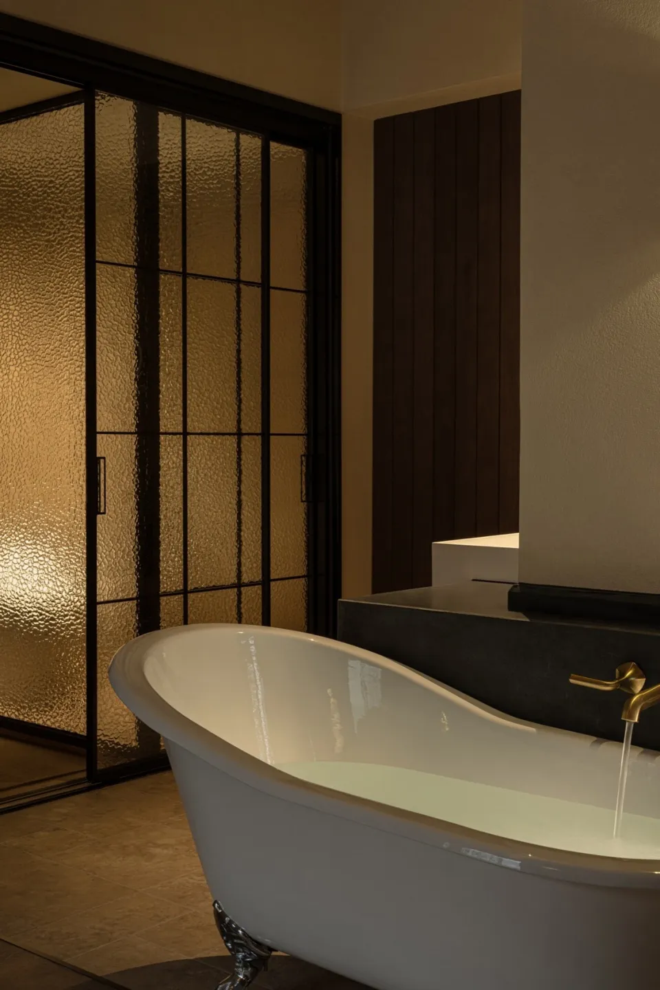 A minimalist bathroom with a white freestanding bathtub and a textured frosted glass sliding door.